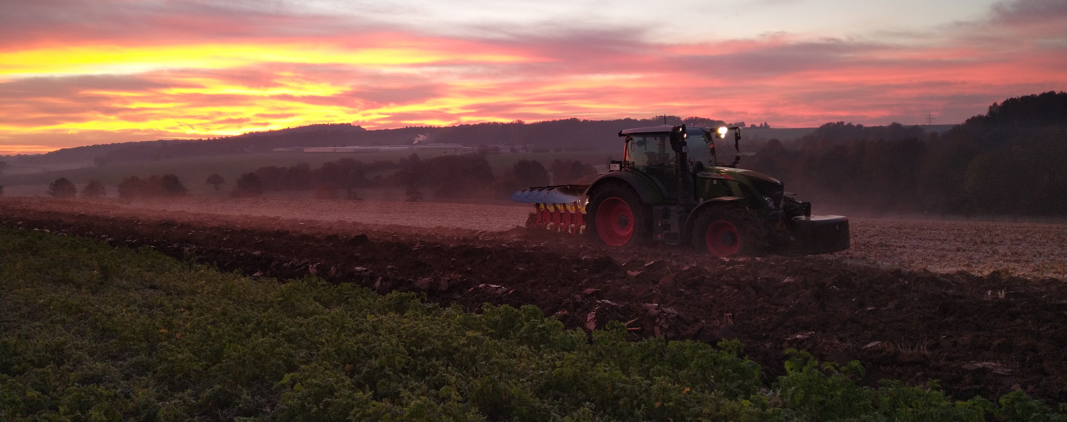 Traktor mit aktiver Beleuchtung bei der Feldarbeit in der Abenddämmerung.